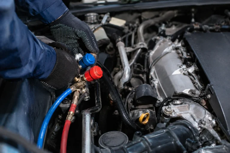 Mechanik podłącza przewody serwisowe do układu klimatyzacji w komorze silnika samochodu.