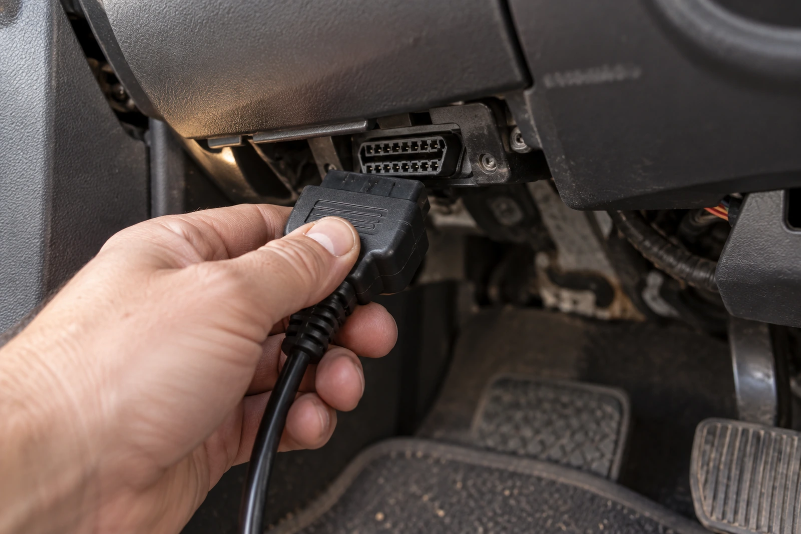 Podłączanie interfejsu diagnostycznego do gniazda OBD2 pod kierownicą samochodu.